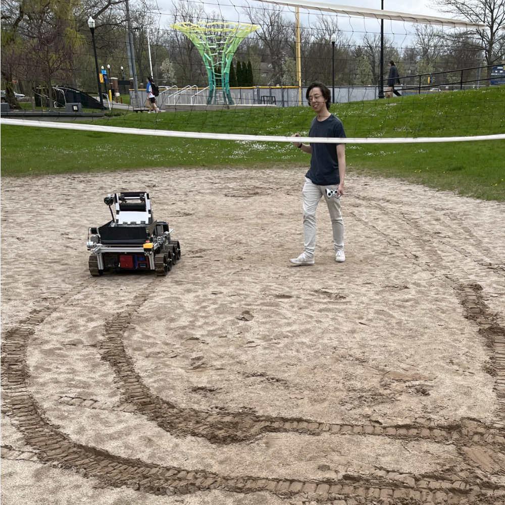 Rochester undergraduate student tests the Melbot V3 lunar rover on an outdoor campus volleyball field.